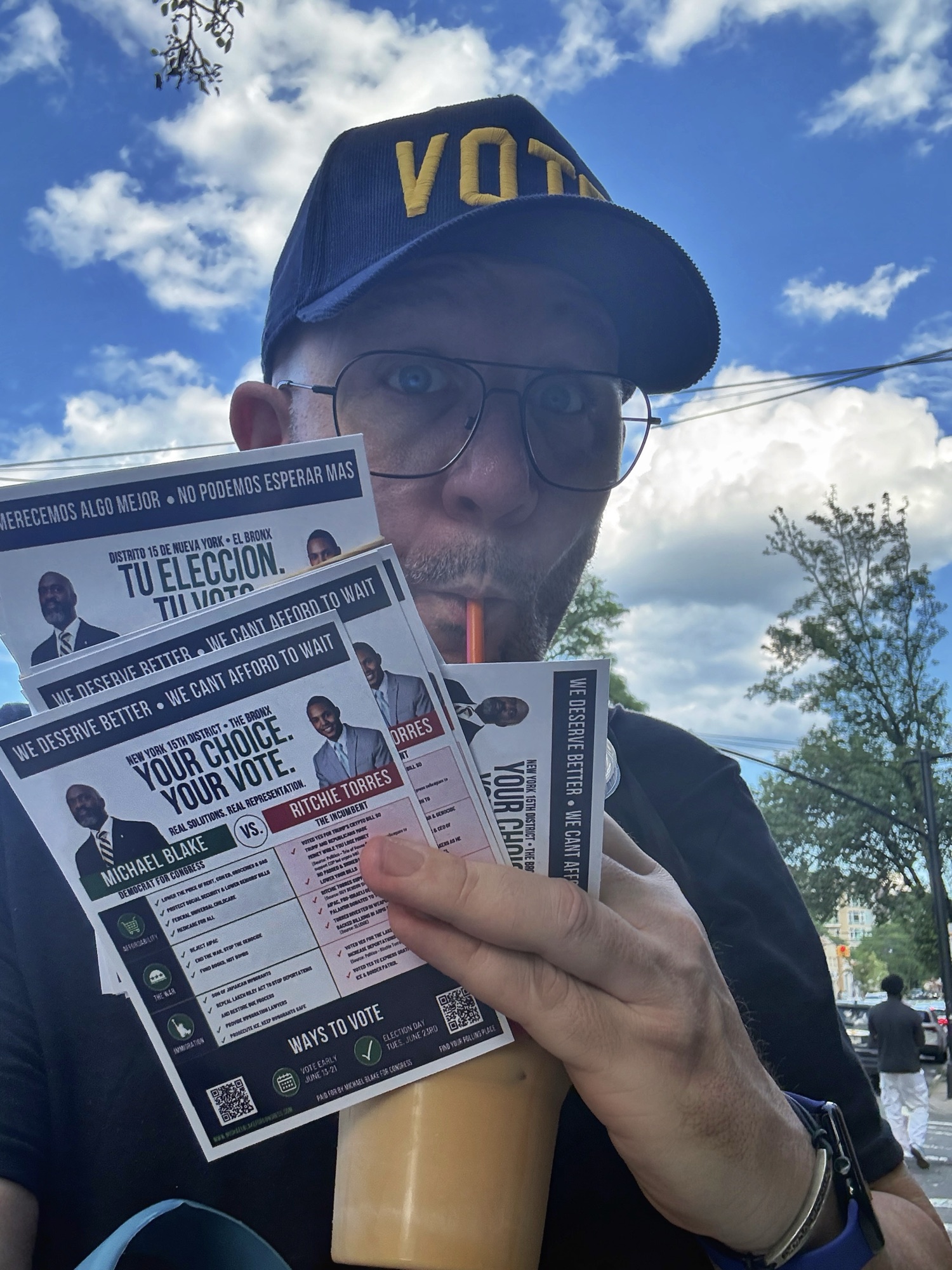 Blue Moreno holding a voting information flyer beneath a VOTE cap outdoors