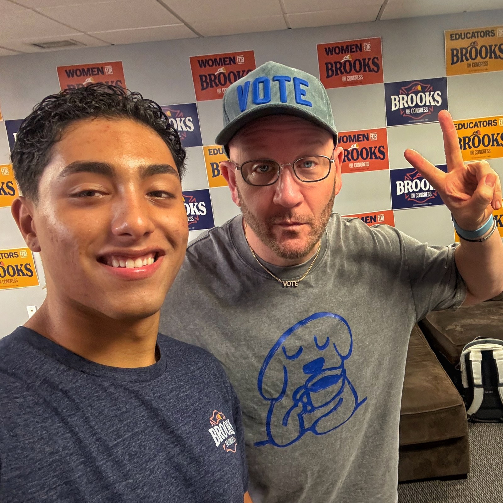 Blue Moreno giving a peace sign beside a man in front of Brooks for Congress signs in Pennsylvania