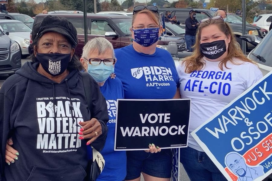 Four Georgia volunteers holding Vote Warnock and Warnock and Ossoff campaign signs